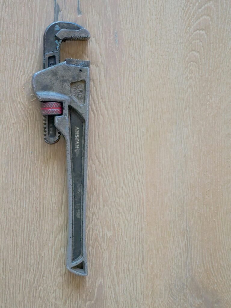 Close-up of a metal plumber's wrench against a wooden surface, showcasing tool detail.